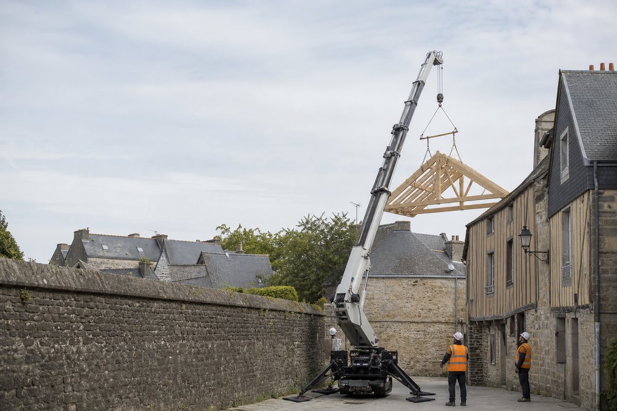 Mise en situation d’un mini-grue araignée avec une équipe de levage pour charpente dans la ville close, dans un environnement inspiré de Vannes