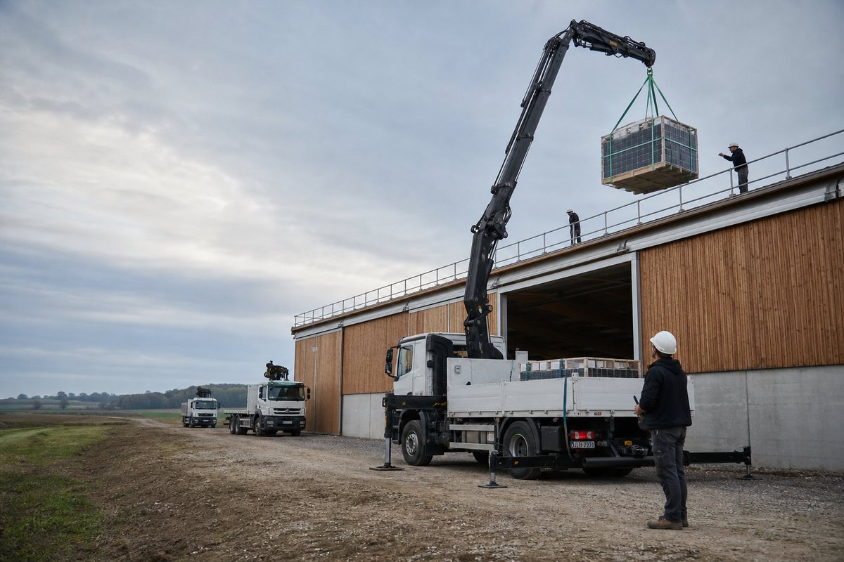 Camion-grue livrant des panneaux photovoltaïques sur un hangar
